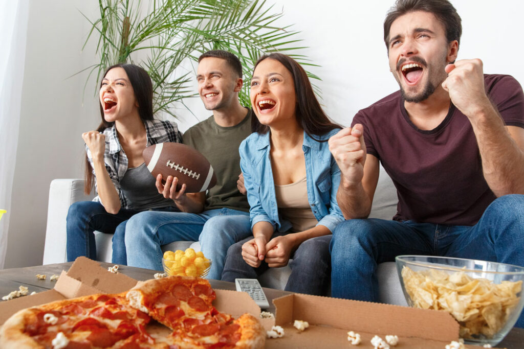 Friends sitting on a couch eating pizza and cheering